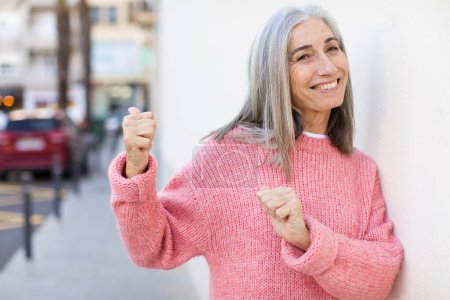 Foto de Senior jubilado bastante blanco cabello mujer sonriendo alegremente y casualmente apuntando a copiar el espacio en el lado, sintiéndose feliz y satisfecho - Imagen libre de derechos