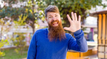 Photo for Red hair bearded man smiling happily and cheerfully, waving hand, welcoming and greeting you, or saying goodbye - Royalty Free Image