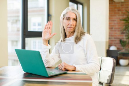 Photo for Senior pretty woman looking serious showing open palm making stop gesture with a laptop - Royalty Free Image