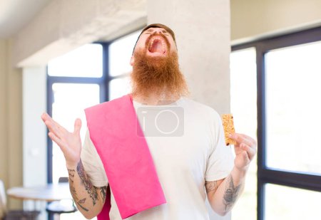 Photo for Red hair man screaming with hands up in the air with a cereal bar. fitness concept - Royalty Free Image