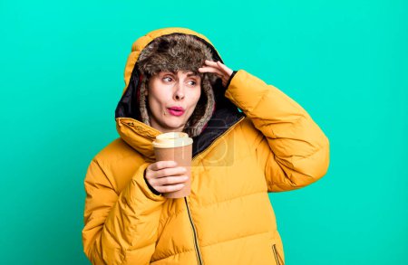 Foto de Young adult pretty woman wearing anorak and winter hat and holding a take away coffee - Imagen libre de derechos