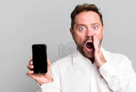 Photo for Middle age man feeling shocked and scared. showing a smartphone - Royalty Free Image