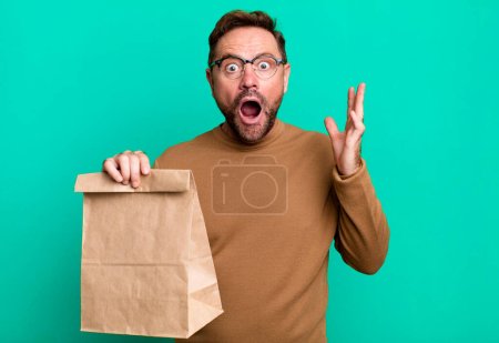 Foto de Hombre de mediana edad se siente muy sorprendido y sorprendido. llevar bolsa de papel - Imagen libre de derechos