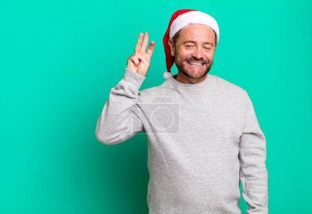 Téléchargez les photos : Homme d'âge moyen souriant et l'air amical, montrant numéro trois. concept de Noël - en image libre de droit