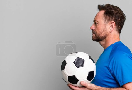 Foto de Hombre de mediana edad en vista de perfil pensando, imaginando o soñando despierto. con una pelota de fútbol. concepto de fitness - Imagen libre de derechos
