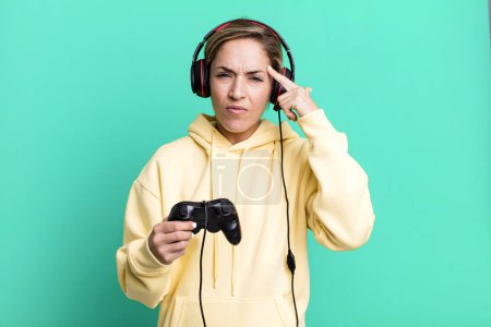 Photo for Pretty blonde woman feeling confused and puzzled, showing you are insane. gamer with headset and a controller - Royalty Free Image
