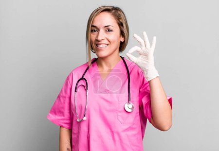 Photo for Pretty blonde woman feeling happy, showing approval with okay gesture. nurse concept - Royalty Free Image
