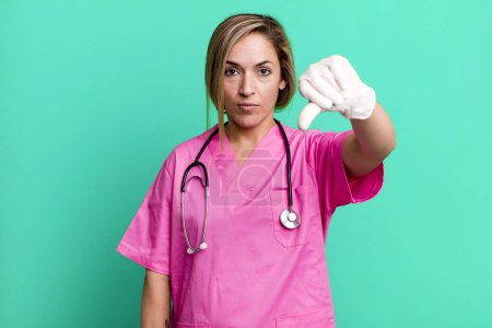 Photo for Pretty blonde woman feeling cross,showing thumbs down. nurse concept - Royalty Free Image