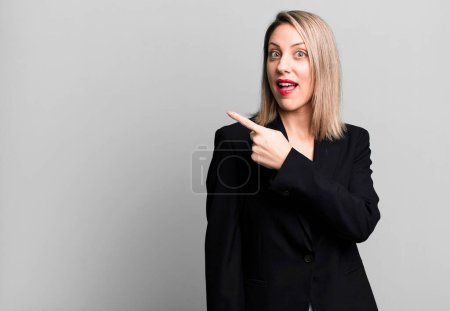 Foto de Mujer rubia bonita mirando emocionada y sorprendida señalando a un lado. concepto de mujer de negocios - Imagen libre de derechos