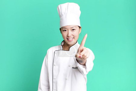 Téléchargez les photos : Jolie femme asiatique souriant fièrement et en toute confiance faisant numéro un. concept de chef restaurant - en image libre de droit