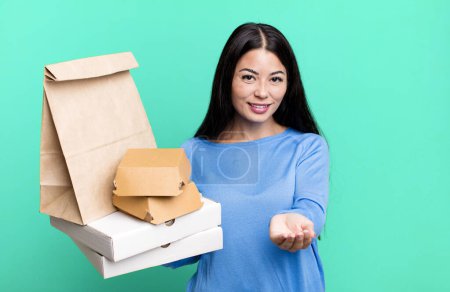 Foto de Mujer bonita hispana sonriendo felizmente con amigable y ofreciendo y mostrando un concepto. con paquetes de comida rápida para llevar - Imagen libre de derechos