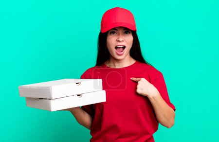 Photo for Hispanic pretty woman looking shocked and surprised with mouth wide open, pointing to self. delivery pizza concept - Royalty Free Image