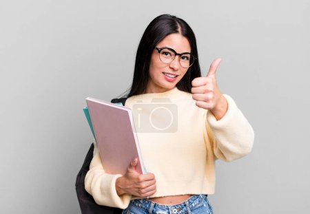 Téléchargez les photos : Hispanique jolie femme se sentant fière, souriant positivement avec les pouces levés. concept étudiant universitaire - en image libre de droit
