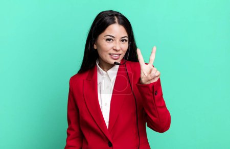 Foto de Hispanic pretty woman smiling and looking friendly, showing number two. telemarketing concept - Imagen libre de derechos