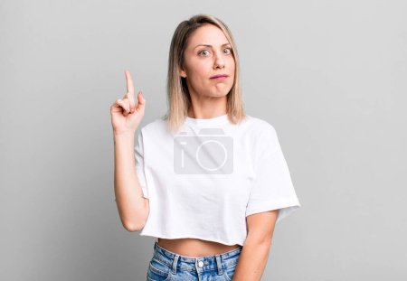 Photo for Blonde adult woman feeling like a genius holding finger proudly up in the air after realizing a great idea, saying eureka - Royalty Free Image