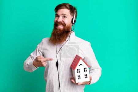 Photo for Young adult red hair bearded cool real state agent man with a house model - Royalty Free Image