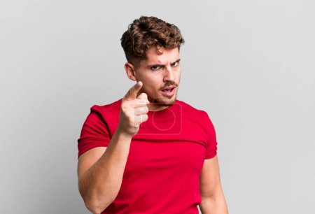 Téléchargez les photos : Young adult caucasian man pointing at camera with an angry aggressive expression looking like a furious, crazy boss - en image libre de droit