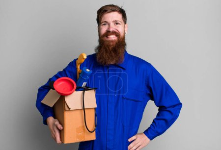 Foto de Hombre de barba larga sonriendo felizmente con una mano en la cadera y confiado. reparador con concepto de caja de herramientas - Imagen libre de derechos