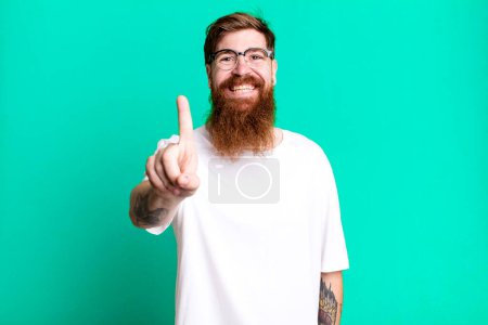 Téléchargez les photos : Barbe longue et cheveux roux homme souriant fièrement et en toute confiance faisant numéro un - en image libre de droit