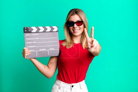 Photo for Young pretty woman smiling and looking friendly, showing number two. film, cinema and movie concept - Royalty Free Image