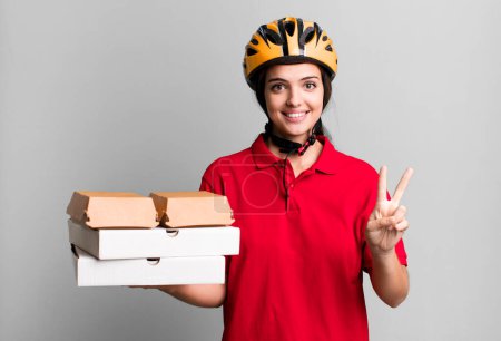 Photo for Young pretty woman smiling and looking happy, gesturing victory or peace. pizza delivery concept - Royalty Free Image