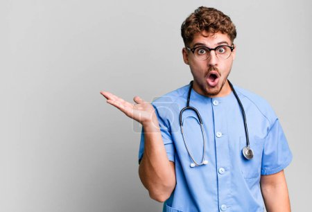 Photo for Young adult caucasian man looking surprised and shocked, with jaw dropped holding an object. nurse concept - Royalty Free Image