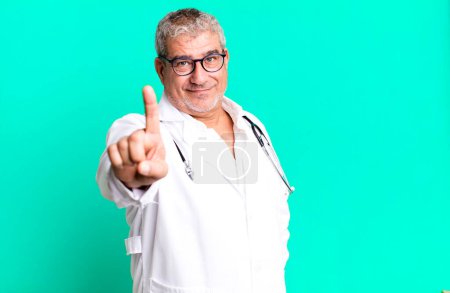 Foto de Hombre mayor de mediana edad sonriendo orgullosamente y con confianza haciendo número uno. concepto médico o médico - Imagen libre de derechos