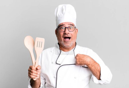 Foto de Hombre mayor de mediana edad sintiéndose feliz y señalándose a sí mismo con una emoción. chef de restaurante con un concepto de herramienta - Imagen libre de derechos