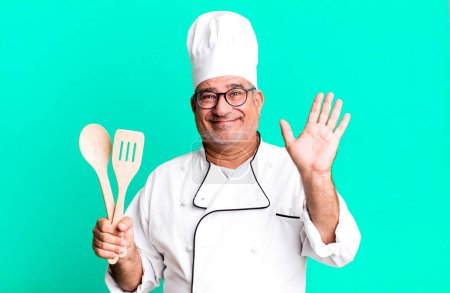 Photo for Middle age senior man smiling happily, waving hand, welcoming and greeting you. restaurant chef with a tool concept - Royalty Free Image