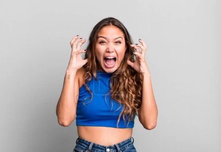 Photo for Young pretty woman screaming with hands up in the air, feeling furious, frustrated, stressed and upset - Royalty Free Image