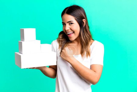 Photo for Hispanic pretty woman feeling happy and facing a challenge or celebrating with blank packages boxes - Royalty Free Image
