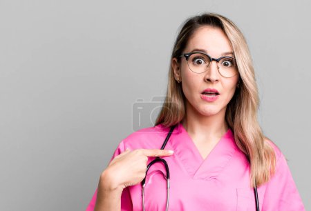Photo for Looking shocked and surprised with mouth wide open, pointing to self. nurse concept - Royalty Free Image
