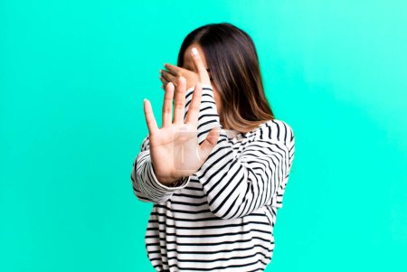 Photo for Hispanic pretty woman covering face with hand and putting other hand up front to stop camera, refusing photos or pictures - Royalty Free Image