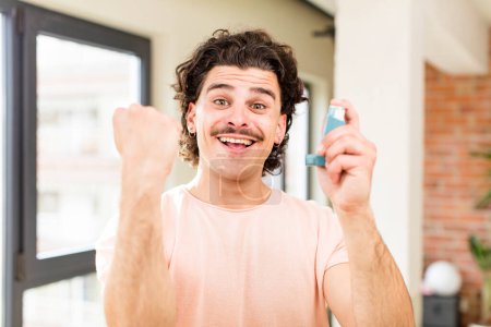 Téléchargez les photos : Jeune homme beau avec un inhalateur d'asthme à l'intérieur de la maison - en image libre de droit