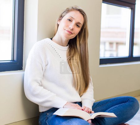Téléchargez les photos : Young adult pretty blonde woman reading a book at home - en image libre de droit
