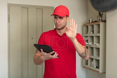 Photo for Young handsome man looking serious showing open palm making stop gesture. delivery man concept - Royalty Free Image