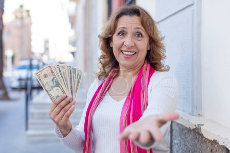 Photo for Middle age pretty woman smiling happily and offering or showing a concept. dollar banknotes concept - Royalty Free Image