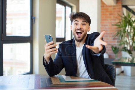Foto de Joven hombre guapo sonriendo alegremente y ofreciendo o mostrando un concepto. concepto de smartphone - Imagen libre de derechos