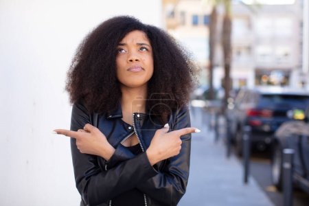 Photo for African american pretty woman looking puzzled and confused, insecure and pointing in opposite directions with doubts - Royalty Free Image