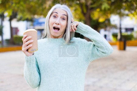Foto de Mujer bastante mayor mirando feliz, asombrado y sorprendido con un café para llevar - Imagen libre de derechos