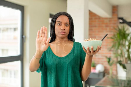 Photo for Black afro woman looking serious showing open palm making stop gesture. breakfast bowl concept - Royalty Free Image