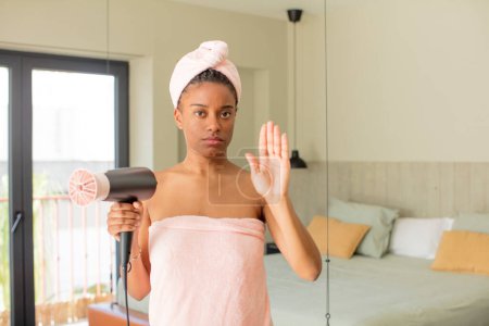 Téléchargez les photos : Afro femme noire regardant sérieux montrant paume ouverte faisant geste d'arrêt. concept de sèche-cheveux - en image libre de droit