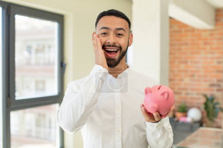 Photo for Young  adult man feeling happy and astonished at something unbelievable. piggybank concept - Royalty Free Image