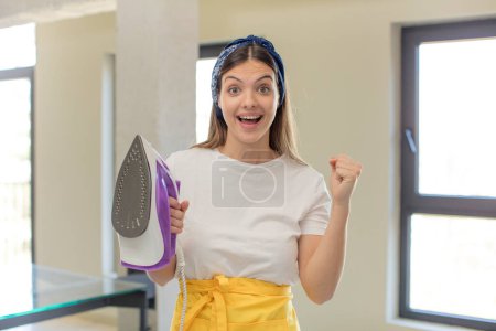 Photo for Young pretty woman feeling shocked,laughing and celebrating success. housekeeper and laundry concept - Royalty Free Image
