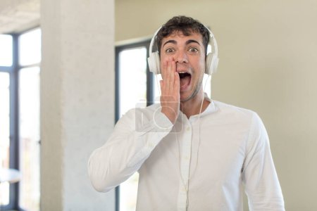 Photo for Young handsome man feeling happy and astonished at something unbelievable. listening music with headphones - Royalty Free Image