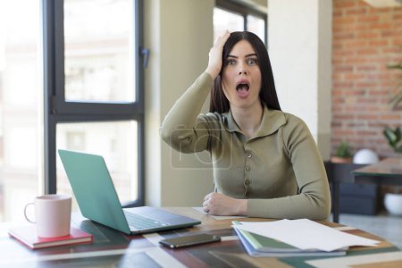 Photo for Pretty young woman feeling extremely shocked and surprised. laptop and desk concept - Royalty Free Image