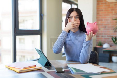 Photo for Pretty young woman covering mouth with a hand and shocked or surprised expression. piggy bank concept - Royalty Free Image
