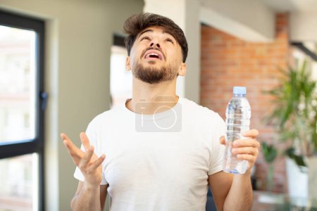 Téléchargez les photos : Jeune homme beau criant avec les mains en l'air. concept de bouteille d'eau - en image libre de droit