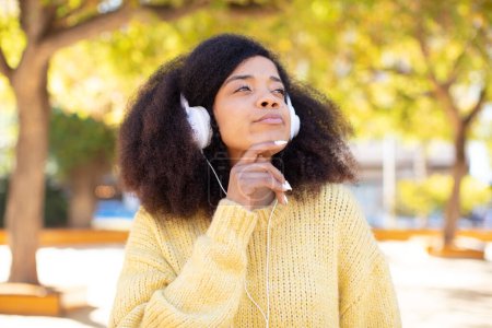 Foto de Bonita mujer negra afro sonriendo con una expresión feliz y segura con la mano en la barbilla. escuchar música con auriculares - Imagen libre de derechos