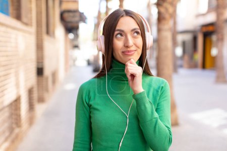 Foto de Smiling with a happy, confident expression with hand on chin. listening music with headphones - Imagen libre de derechos